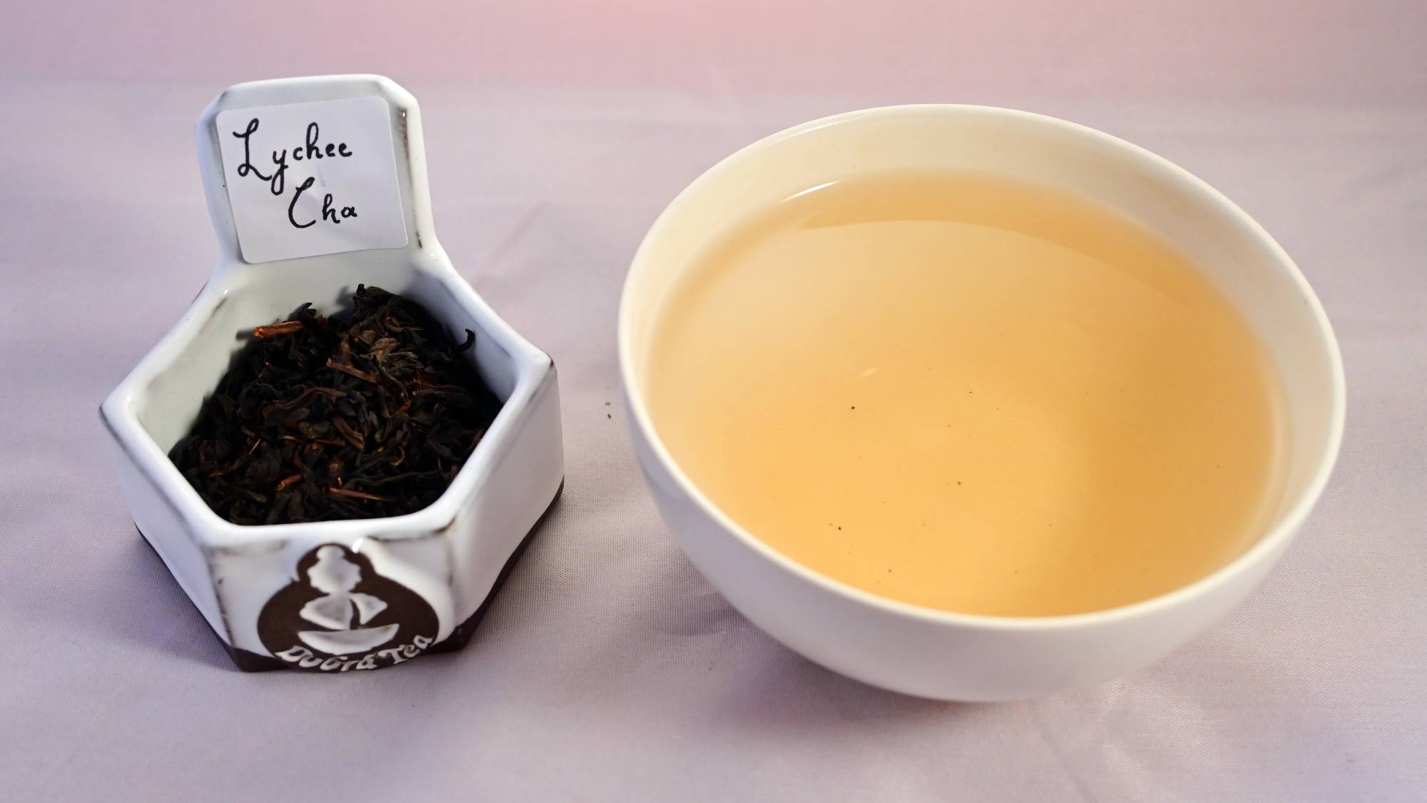 A side by side comparison of Lychee Cha leaves and steeped tea. On the left, the leaves are black and dark brown. On the right, the steeped tea is a vibrant yellow.