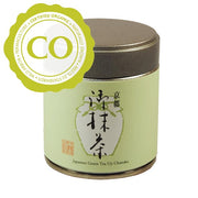 A small metal canister about the size of a human palm. It has a brown lid that can lift off and a pale green body. It on the body is an image of a jar with Japanese characters and a red production stamp. It says "Japanese Green Tea Uji Chanoka" in English below. A sticker labels the tea as Certified Organic.