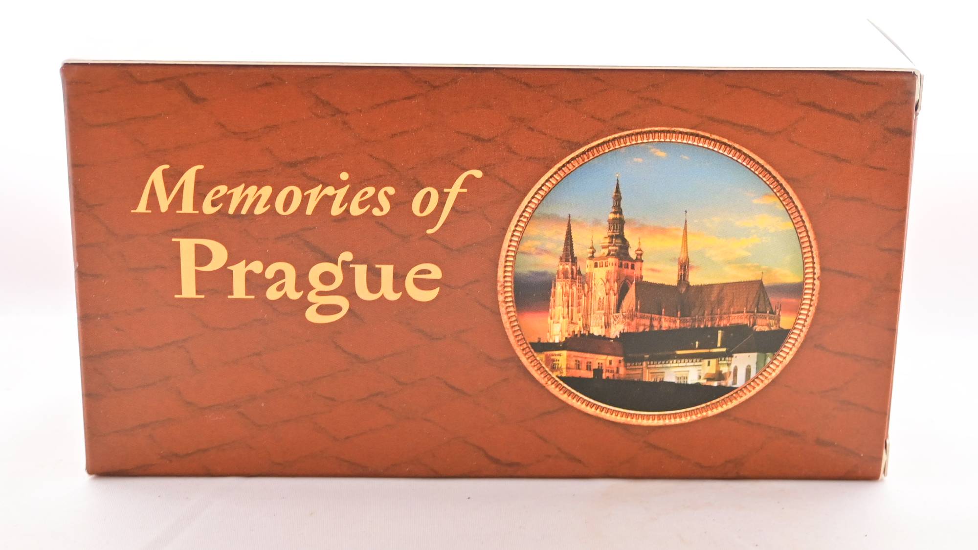 The Memories of Prague paper box is brick-red with a shingled pattern across it. Inside a circle toward the right, a magnificent cathedral is featured against a sunset. Text reads: "Memories of Prague."