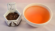 A side-by-side comparison of the Memories of Prague blend and steeped tea. On the left, the blend features tiny black tea pellets with crushed bits of dark chocolate. On the right, the steeped tea is a deep orange color.