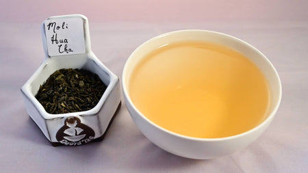 A combination of leaves and a steeped tea cup. The leaves are dark green and appear slightly crumbled. The steeped tea is a red-caramel color.