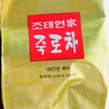 A close-up of the inner Nok Cha plastic tea package. It is golden, with alternating light and dark squares each holding the same set of Korean letters featured in white text inside a centered red box.