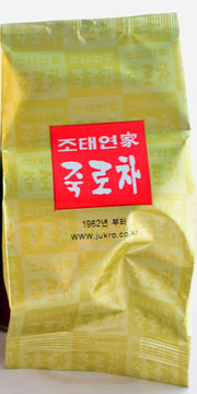 A close-up of the inner Nok Cha plastic tea package. It is golden, with alternating light and dark squares each holding the same set of Korean letters featured in white text inside a centered red box.