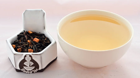 A side-by-side comparison of Plum Tea leaves and steeped tea. On the left, black tea leaves encircle nuggets of orange-colored dried plum. On the right, the liquid is a soft yellow color.