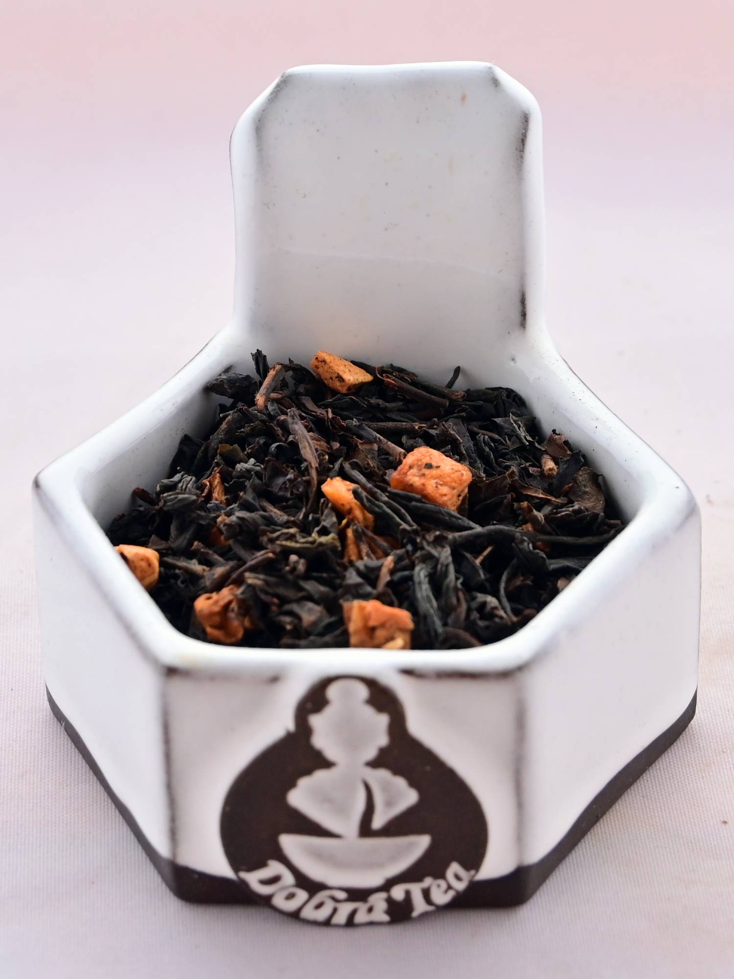 A close-up of Plum Tea leaves. Black and dark brown tea leaves that are partially rolled cling together around cubes of dried plum.