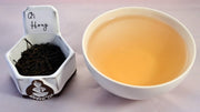 A side-by-side comparison of Qi Hong Mao Feng leaves and steeped tea. On the left, the leaves are small, tightly curled, and black. On the right, the steeped liquid is a soft orange.