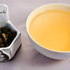 A side-by-side comparison of Sakuracha leaves and a cup of brewed tea. The leaves are whole and curled in on themselves. The steeped liquid is vibrant yellow.
