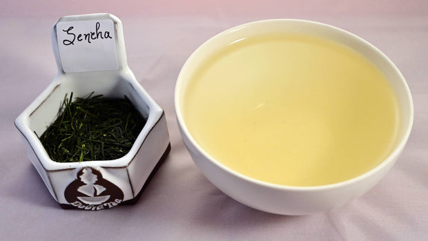 A picture of tea leaves  on the left with steeped tea on the right. The tea leaves are deep green, short, and needle-thin. The tea is pale yellow.