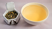 A side-by-side comparison of the Serenitea blend and steeped tisane. On the left, the herbal blend prominently features lavender, chamomile, and tulsi. On the right, the steeped tisane is light orange.