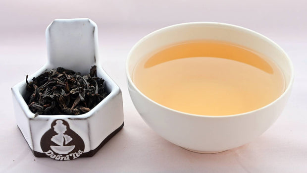A side-by-side comparison of Wuyi Shan Shui Xian leaves and steeped tea. On the left, the leaves are dark brown and swirled into loose spirals. On the right, the steeped liquid is pale orange.