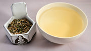 A side-by-side comparison of the Somnolence blend and steeped tisane. On the left, the blend prominently features Valerian root and lavender. On the right, the steeped tisane is a pale yellow.