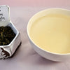 A side-by-side comparison of Tie Guan Yin leaves and steeped tea. The leaves are a light green, and scrunched together into small, wrinkled pebbles. On the right, the steeped liquid is pale peach.