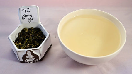 A side-by-side comparison of Tie Guan Yin leaves and steeped tea. The leaves are a light green, and scrunched together into small, wrinkled pebbles. On the right, the steeped liquid is pale peach.