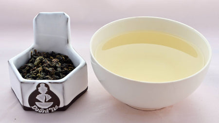A side-by-side comparison of Tung Ting leaves and steeped tea. On the left, the leaves are dark green and have been scrunched and rolled together into pebble-like shapes. On the right, the steeped liquid is a pale yellow.