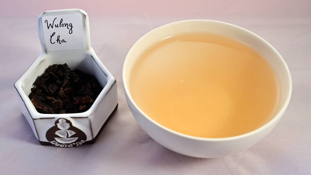 A side-by-side comparison of Wu Long Cha leaves and steeped tea. On the left, the leaves are dark brown and curled into tight, wrinkled pellets. On the right, the steeped liquid is a warm orange.