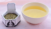 A side-by-side comparison of the dried Yerba Mate herb and steeped tisane. On the left, the leaves are small, flat, and relatively circular. They range in color from pale brown to green-brown. On the right, the steeped tisane is a deep yellow.