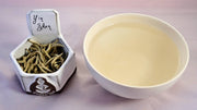 A side by side comparison of Yin Zhen leaves and steeped tea. On the left, the leaves are yellowed and loosely curled. On the right, the steeped tea is a pale yellow.