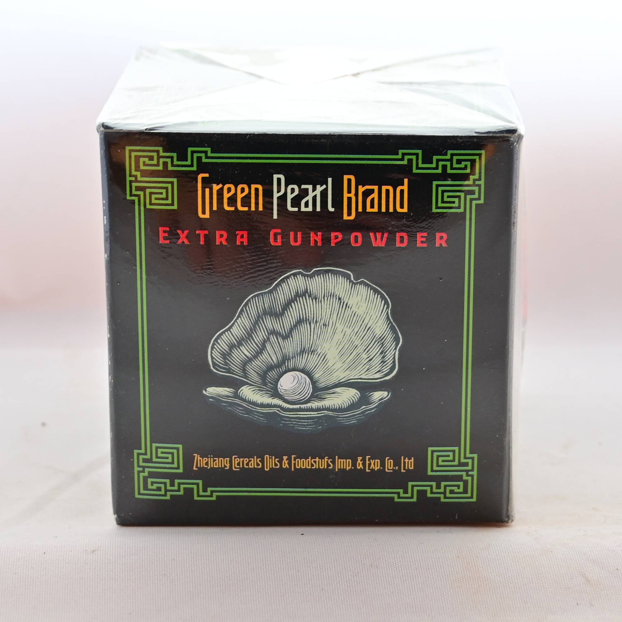 A tea box with text: Green Pearl Brand Extra Gunpowder. There is a line-art oyster with pearl in the center. It is wrapped in plastic.
