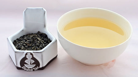 A side-by-side comparison of Zhu Cha leaves and steeped tea. On the left, the leaves are dark green, and resemble small, smooth pellets. On the right, the steeped liquid is a soft gold.
