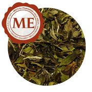 A close up of tea leaves. Most are green, with a slight brown tint. They are crisp and brittle. There is a Meets EU Standards label in the top left.