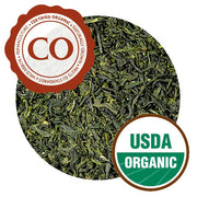 A close-up of Tamaryokucha leaves, showing thin, dark green leaves with a hard sheen on them.  They have Certified Organic and USDA Organic certifications.